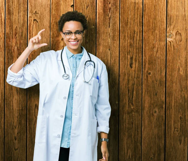 Young african american doctor woman wearing medical coat over isolated background smiling and confident gesturing with hand doing size sign with fingers while looking and the camera. Measure concept.