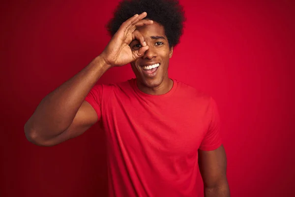 年轻的美国男子与Afro头发穿着T恤站在孤立的红色背景做Ok手势与手微笑 眼睛透过手指与快乐的脸 — 图库照片