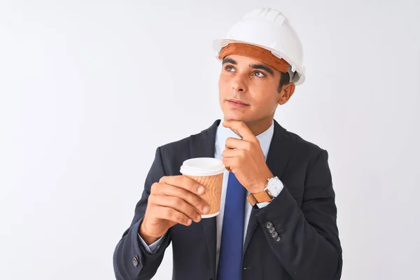 Young handsome architect man wearing helmet drinking coffee over isolated white background serious face thinking about question, very confused idea