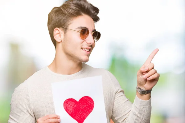 Homem Bonito Jovem Segurando Cartão Com Coração Vermelho Sobre Fundo — Fotografia de Stock
