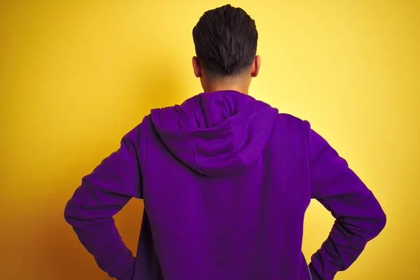 孤立した黄色の背景の上に立つ紫色のスウェットシャツを着た若いブラジル人男性が 体に腕を向けて後ろ向きに立っている — ストック写真