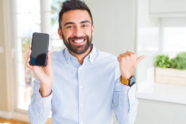スマートフォンの画面を指差し 幸せそうな顔で横に親指で見せるハンサムなヒスパニックビジネスマン — ストック写真