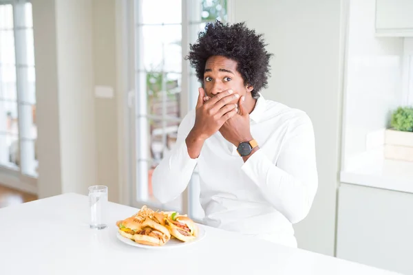 昼食にハンバーガーを食べるアフリカ系アメリカ人の空腹の男は 間違って手で口を覆ってショックを受けました 秘密の概念 — ストック写真