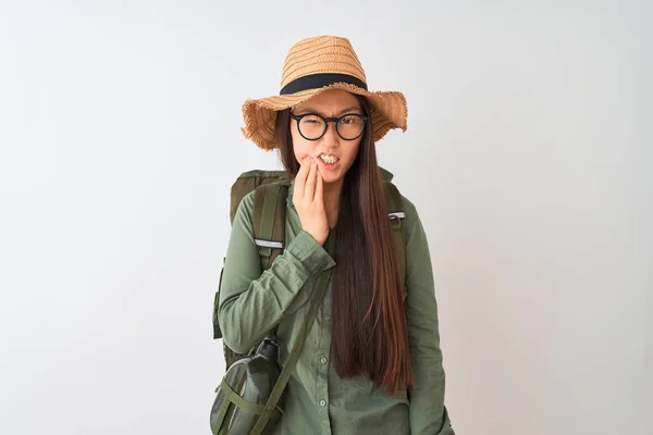 Chinese hiker woman wearing canteen hat glasses backpack over isolated white background touching mouth with hand with painful expression because of toothache or dental illness on teeth. Dentist concept.