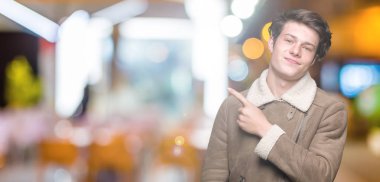 Genç yakışıklı adam giyen kış ceket izole üzerinden reklam, ciddi ve sakin yüz gösterilen yan el parmak ile işaret arka plan