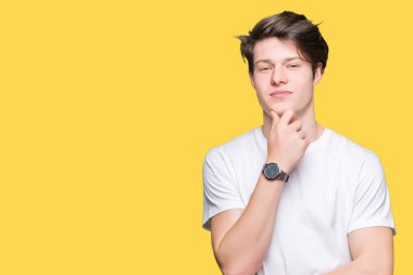 Emin çapraz kollar ve çeneme kaldırdı el ile gülümseme ile kameraya bakarak izole arka plan üzerinde rahat beyaz t-shirt giyen genç yakışıklı adam. Pozitif düşünce.