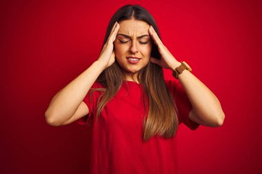 Genç güzel kadın t-shirt giyen stres nedeniyle baş ağrısı için el ile izole kırmızı arka plan üzerinde duran. Acı çeken migren.