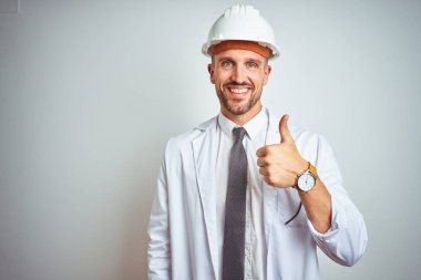 Genç yakışıklı mühendis adam el ile jest kadar mutlu başparmak yapıyor izole arka plan üzerinde emniyet kask giyiyor. Başarı göstererek kameraya bakarak ifadeyi onaylama.