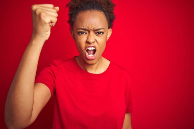 Genç güzel Afrikalı Amerikan kadın üzerinde afro saç ile izole kırmızı arka plan öfkeli ve deli yükseltme yumruk sinirli ve öfkeli çığlık sırasında öfke. Öfke ve agresif kavram.