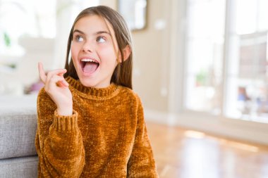 Güzel genç kız çocuk rahat kazak neşeli bir gülümseme ile el ve parmak kadar yan yüzünde mutlu ve doğal ifade ile işaret yüz ile giyiyor