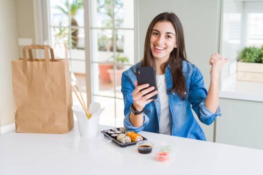 Güzel genç kadın uygulama telefon işaret ve mutlu yüz gülümseyen yan başparmak ile gösteren kullanarak gıda teslim sipariş
