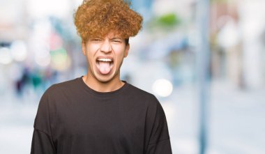 Genç yakışıklı adam ile afro saç giyen siyah t-shirt yapıştırma dil dışarı mutlu ile komik ifade. Duygu konsepti.