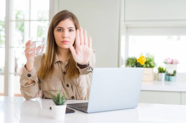 Bilgisayar la çalışan güzel genç kadın ciddi ve kendinden emin ifade, savunma jesti ile dur işareti yapıyor açık el ile su bardağı içmek için bir mola alır