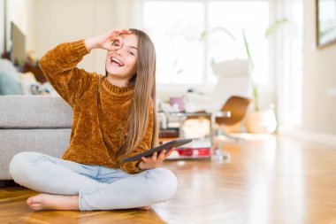 Güzel genç kız çocuk dijital Touchpad tableti kullanarak yerde oturan mutlu yüz gözleri parmak görünümlü el ile ok işareti yapıyor gülümseyen