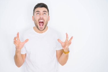 Beyaz izole arka plan çılgın ve deli bağırma ve agresif ifade ve kollar ile bağırarak üzerinde rahat beyaz t-shirt giyen genç yakışıklı adam kaldırdı. Hayal kırıklığı kavramı.