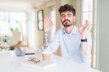 Genç iş adamı rahat çalışan ve gözleri kapalı parmakları ile meditasyon jest yapıyor gülümseyerek. Yoga konsepti.