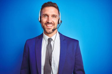 Yüz üzerinde mutlu ve serin bir gülümseme ile mavi izole arka plan üzerinde çağrı merkezi kulaklık giyen genç yakışıklı operatör adam. Şanslı kişi.