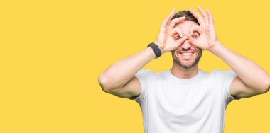 Yakışıklı adam, dilini parmaklarının arasından baktığını yapışmasını dürbün gibi ok jest yapıyor casual beyaz t-shirt giyiyor. Deli ifade.