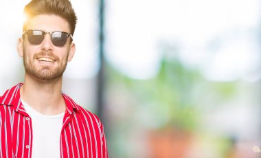 Yakışıklı delikanlı hayrete ve el ile sunulması ve parmak ile işaret ederken kameraya gülümseyen güneş gözlüğü takıyor.