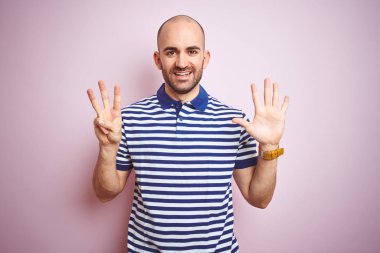 Sakal ile genç kel adam rahat çizgili mavi t-shirt pembe izole arka plan üzerinde gösteren ve parmak sayısı sekiz ile işaret kadar emin ve mutlu gülümseyen.