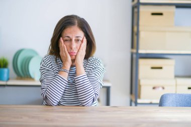 Evde masada oturan orta yaş yaşlı kadın Yorgun eller yüz kapsayan, depresyon ve üzüntü, üzgün ve sorun için rahatsız