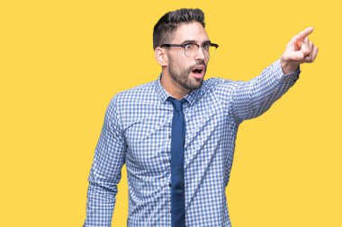 Üzerinde gözlük takan genç iş adamı izole arka plan ile sürpriz devam parmakla, açık ağız hayret ifadesi, önünde bir şey