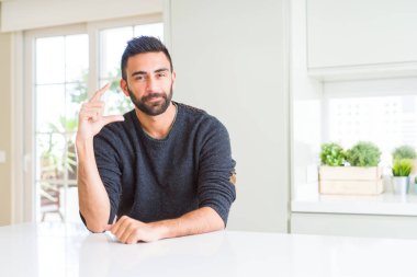 Yakışıklı İspanyol adam ev gülümseyen ve kendine güvenen rahat kazak giyen el ile boyutu işareti yaparken parmaklar ve kamera bakıyor. Ölçü kavramı.