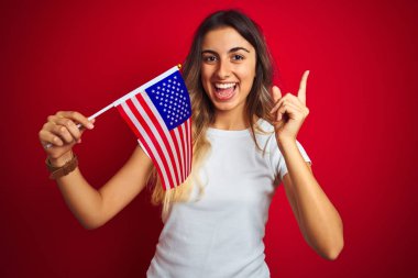 Kırmızı izole arka plan üzerinde Amerika Birleşik Devletleri bayrağı tutan genç kadın çok mutlu yan el ve parmak ile işaret