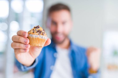 Yakışıklı adam çikolata cips muffin yeme gurur çığlık ve zafer ve başarı çok heyecanlı kutluyor, duygu tezahürat