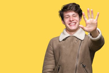 Gösterilen arka plan üzerinde kış ceket giyen genç yakışıklı adam izole ve parmakları ile işaret kendinden emin ve mutlu gülümseyerek süre beş numara.
