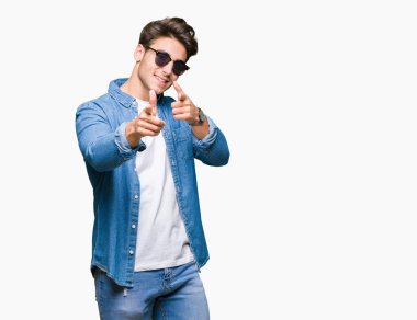 Genç yakışıklı adam kameraya mutlu ve komik suratla parmakları işaret izole arka plan üzerinde güneş gözlüğü takıyor. İyi enerji ve vibes.