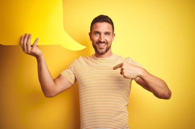 Sürpriz yüz kendini işaret parmak ile sarı izole arka plan üzerinde mesaj için boş konuşma balonu tutan genç adam