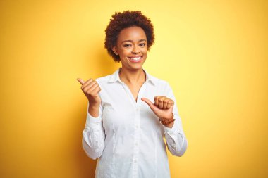 İzole sarı arka plan üzerinde Afrikalı Amerikan iş kadını arka arkaya el ve başparmak yukarı Işaret, gülümseyen emin