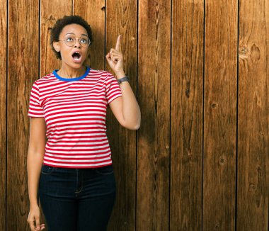 Başarılı fikirle izole arka plan işaret parmağı üzerinde gözlük takan güzel genç Afro-Amerikan kadın. Çıktıktan ve mutlu. Bir numara.