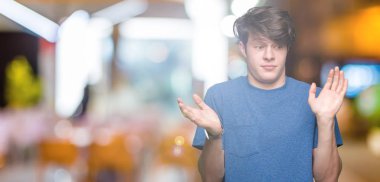 Üzerinde mavi t-shirt giyen genç yakışıklı adam arka plan clueless ve şaşkın bir ifadeyle kollar ve eller kaldırdı izole. Şüphe kavramı.