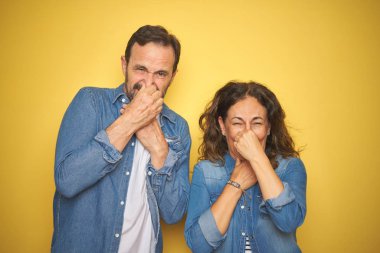 Güzel orta yaş çift birlikte izole sarı arka plan üzerinde kot gömlek giyen bir şey kokulu ve kokulu, dayanılmaz koku, burun parmakları ile nefes tutarak. Kötü kokular kavramı.
