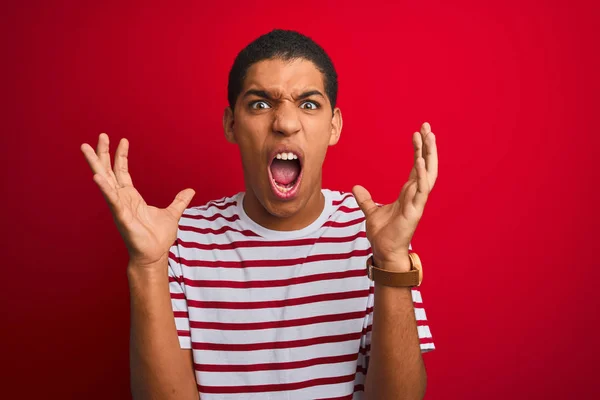 年轻的英俊阿拉伯男子穿着条纹T恤在孤立的红色背景疯狂和疯狂的喊叫和大喊 咄咄逼人的表情和手臂提高 挫折概念 — 图库照片
