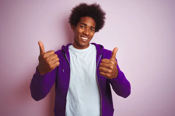 孤立したピンクの背景の上に立つ紫色のスウェットシャツを着た若いアフリカ系アメリカ人男性は 手でポジティブなジェスチャーを行い 親指を笑顔で幸せにします 陽気な表情と勝者のジェスチャー — ストック写真
