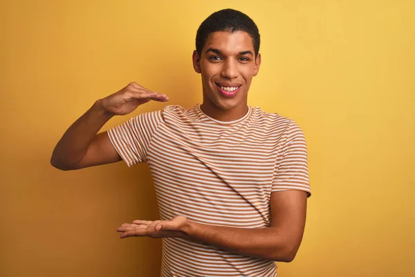 年轻英俊的阿拉伯男子穿着条纹T恤站在孤立的黄色背景手势与双手显示大尺寸的标志 测量符号 微笑着看着相机 测量概念 — 图库照片
