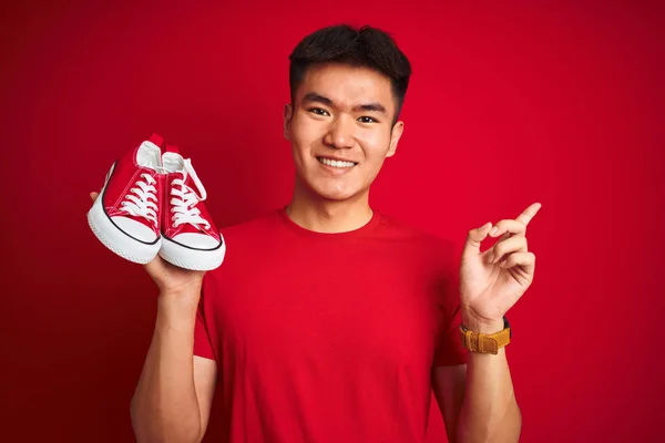 Jovem Asiático Chinês Homem Segurando Casual Tênis Sobre Isolado Vermelho — Fotografia de Stock