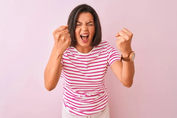 孤立したピンクの背景の上に立つストライプのTシャツを着た若い美しい女性は怒りで叫びながら 怒りと怒りで叫びながら 怒りと怒りを上げ 怒りと怒りを上げる拳を上げました 怒りとアグレッシブなコンセプト — ストック写真