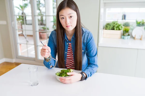 真剣に考えるスマートな顔に自信のある表情で緑の新鮮なブロッコリーを食べる美しいアジアの女性 — ストック写真