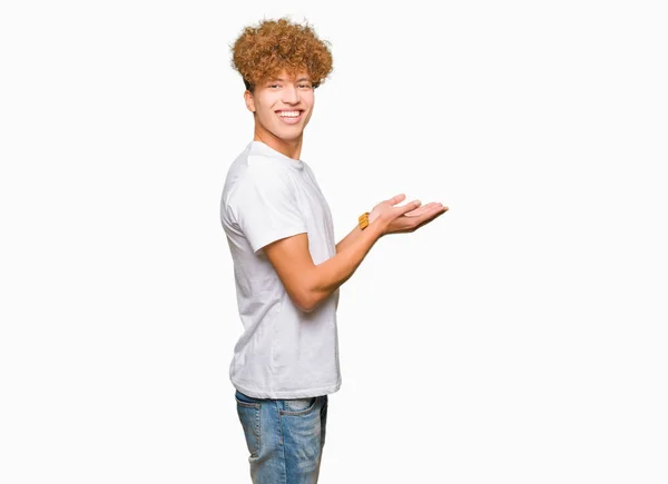 カジュアルな白い シャツを身に着けているアフロの髪の若いハンサムな男が手と開いた掌で側面を指し 広告を笑顔で幸せにし 自信を持っている — ストック写真