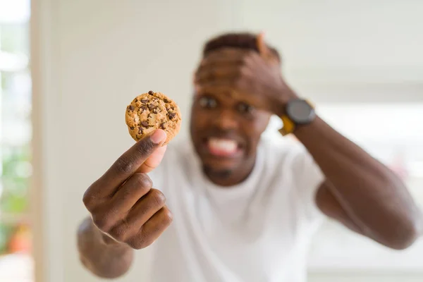Joven Afroamericano Comiendo Galletas Fritas Chocolate Estresado Con Mano Cabeza — Foto de Stock
