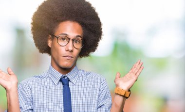 Gözlük clueless ve şaşkın bir ifadeyle kollar ve eller kaldırdı giyen afro saçlı genç Afro-Amerikalı iş adamı. Şüphe kavramı.