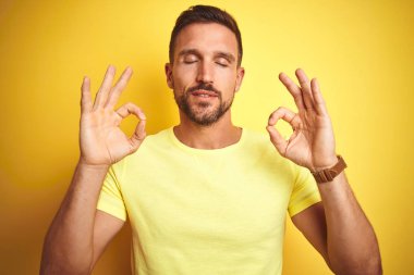 Sarı izole arka plan üzerinde rahat sarı t-shirt giyen genç yakışıklı adam Relax ve gözleri ile gülümseyen meditasyon jest parmaklar ile kapalı. Yoga konsepti.