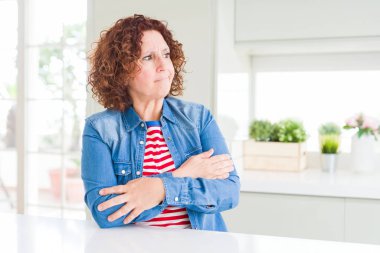 Kıvırcık saçlı orta yaş yaşlı kadın evde kot ceket giyen kolları ile yan bakarak ikna ve kendinden emin geçti