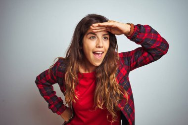 Beyaz izole arka plan üzerinde ayakta kırmızı t-shirt ve ceket giyen genç güzel kadın çok mutlu ve gülümsüyor uzağa baş el ile bakıyor. Arama konsepti.