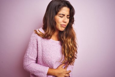 Genç güzel kadın bulantı, ağrılı hastalık hissi nedeniyle mide el ile pembe izole arka plan üzerinde ayakta kazak giyiyor. Ağrı kavramı.