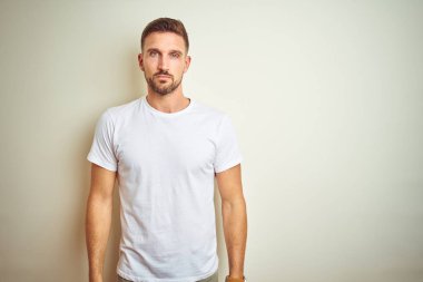 Üzerinde rahat beyaz t-shirt giyen genç yakışıklı adam arka plan gevşek yüzünde ciddi bir ifade ile izole. Basit ve doğal kameraya bakıyor.